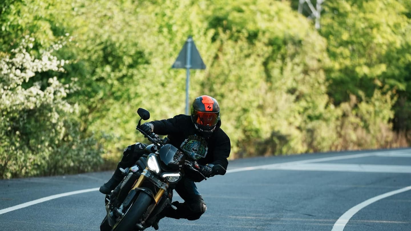 Motorista inclinant una moto esportiva en una corba boscosa, equipat amb casc i jaqueta