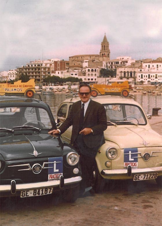Lluís Puig Casanovas, fundador de Autoescuela Palamós, con dos coches de prácticas en el puerto de Palamós